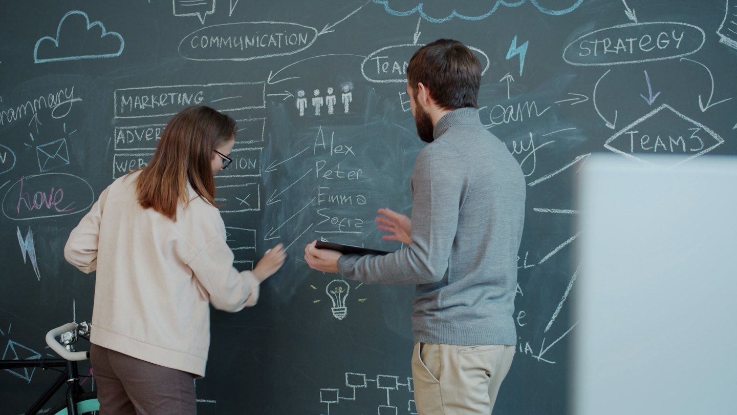 Two colleagues brainstorming marketing strategy on a large chalkboard.