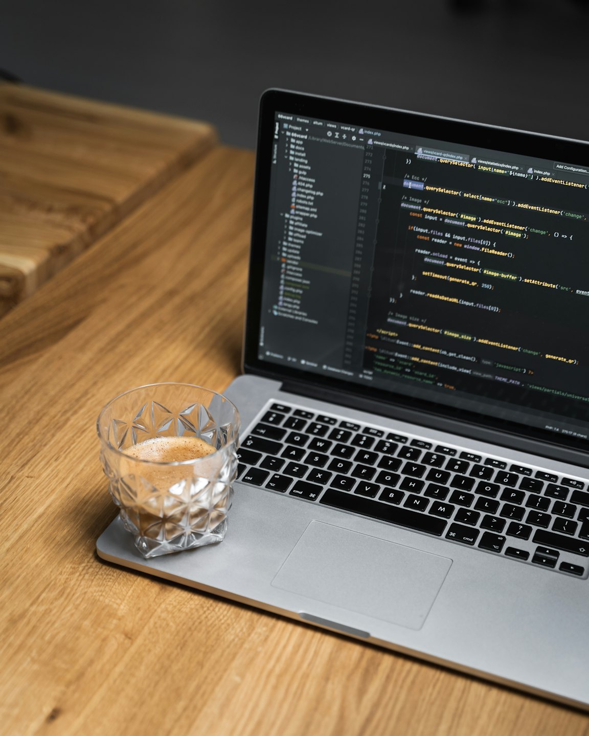 Laptop displaying code on a wooden desk with an espresso.