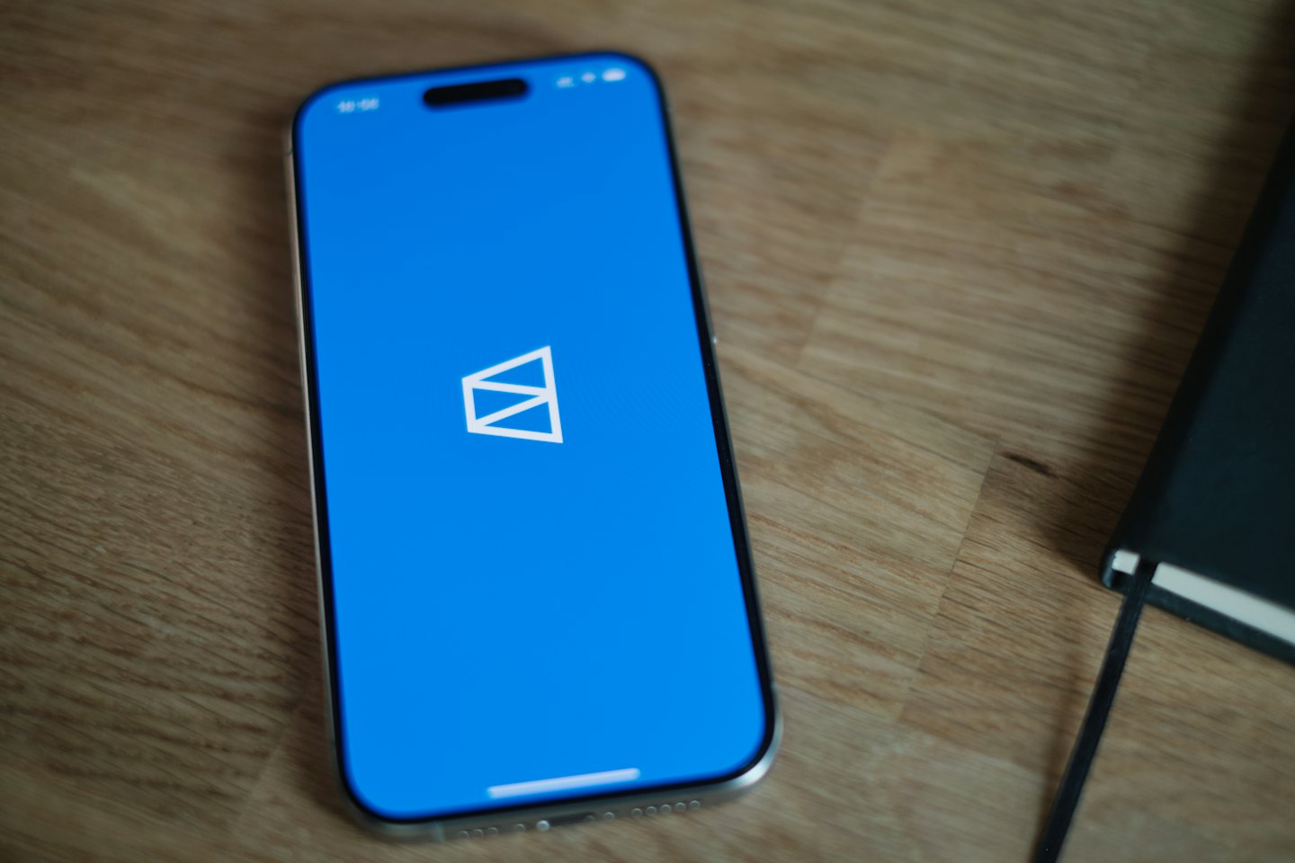 Smartphone with a geometric logo resting on a wooden desk.